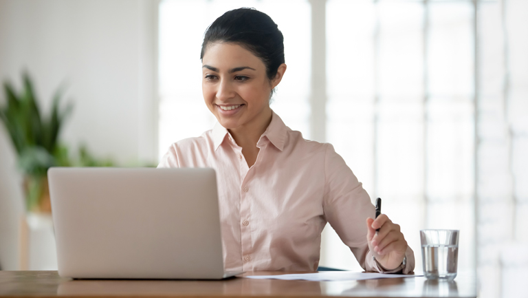 businesswoman sitting at desk in office working online on laptop busy with paperwork